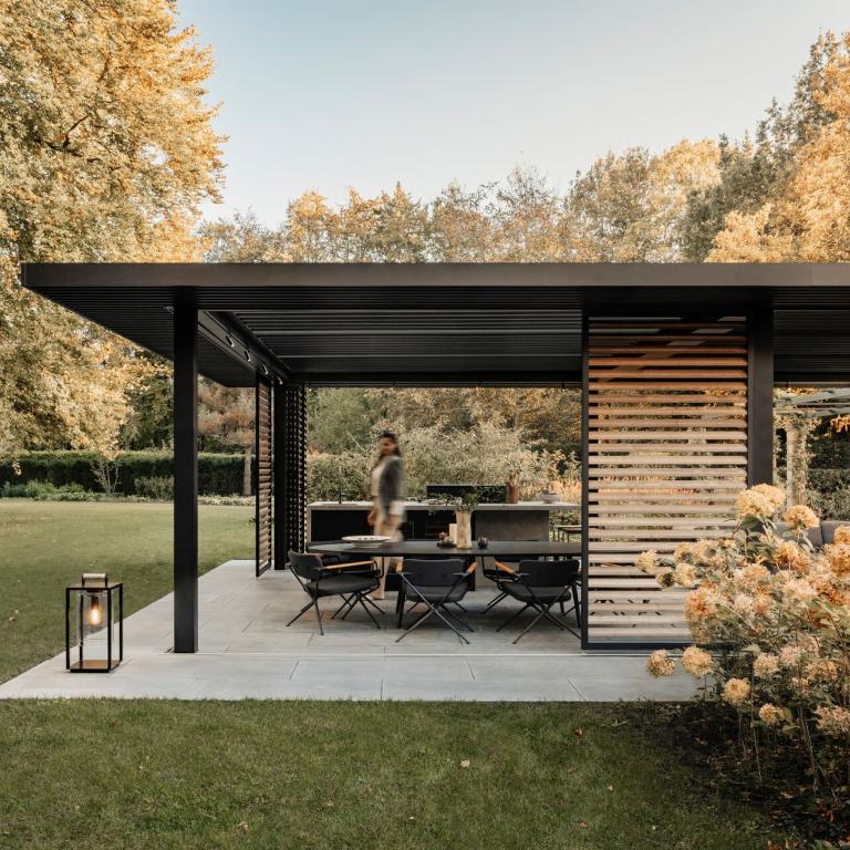 Amani by Renson verkrijgbaar bij Demaeght bv uit Waregem en Oostrozebeke. Een overkapping met beweegbare lamellen in een zwarte structuur met aluminium oversteek en houten verschuifbare lamellen. Dit is volledig op maat. 
