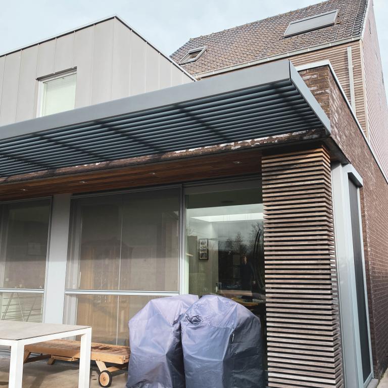 Renson Sunclips structurele zonwering geplaatst aan deze gerenoveerde woning te Anzegem. De aluminium lamellen passen naadloos bij het hout van de gevelbekleding. Een modern en strak design
