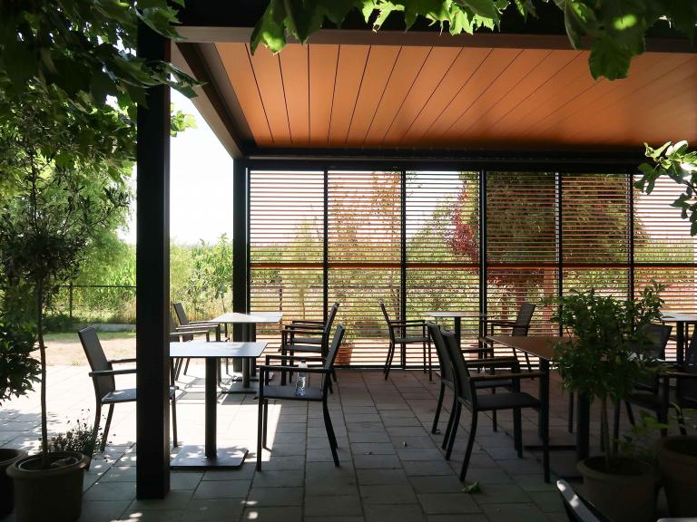 Demaeght Zonwering en interieur plaatste deze Renson Camargue terrasoverkapping aan restaurant La Barriga uit de Pinte. Een modern en strak design tegen een witte crepi gevel van Belgische kwaliteit. Houten schuifpanelen en een aluminium pergola.