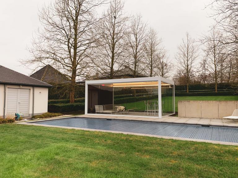 Renson Camargue terrasoverkapping geplaatst op deze mooie locatie te Anzegem als poolhouse aan een zwembad. Met zijn houten achterwand, glazen schuifwanden, led-verlichting en verwarming is dit een full Option lamellendak.